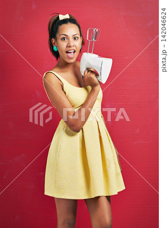 Happy woman, portrait and baker with electric mixer for ingredients or desert on a red studio background. Young female person with surprise for home appliance, baking or hospitality in yellow dress Happy woman, portrait and baker with electric mixer for ingredients or desert on a red studio background. Young female person with surprise for home appliance, baking or hospitality in yellow dress 142046624