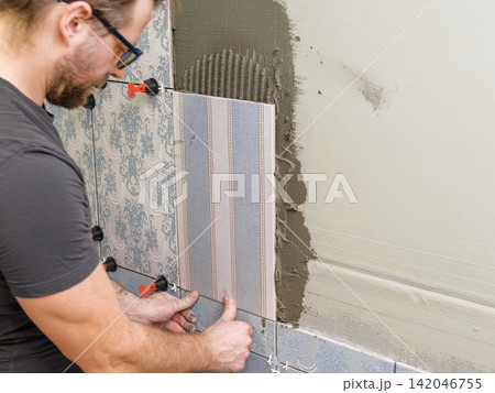 Worker Laying Ceramic Tiles on the Wall. Repairman Placing White Gray Square Tiles, Applying Adhesive. Builder Installing Tile Using Leveler, Tile Leveling Clips. Tiling. Finishing Repair Work. 4K Worker Laying Ceramic Tiles on the Wall. Repairman Placing White Gray Square Tiles, Applying Adhesive. Builder Installing Tile Using Leveler, Tile Leveling Clips. Tiling. Finishing Repair Work. 4K 142046755