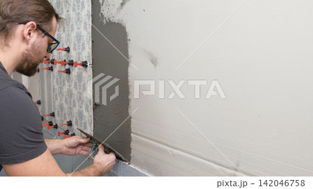 Worker Laying Ceramic Tiles on the Wall. Repairman Placing White Gray Square Tiles, Applying Adhesive. Builder Installing Tile Using Leveler, Tile Leveling Clips. Tiling. Finishing Repair Work. 4K Worker Laying Ceramic Tiles on the Wall. Repairman Placing White Gray Square Tiles, Applying Adhesive. Builder Installing Tile Using Leveler, Tile Leveling Clips. Tiling. Finishing Repair Work. 4K 142046758