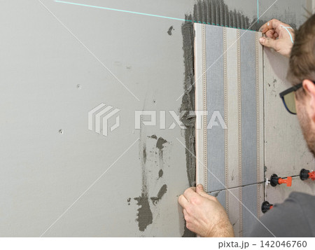 Worker Laying Ceramic Tiles on the Wall. Repairman Placing White Gray Square Tiles, Applying Adhesive. Builder Installing Tile Using Leveler, Tile Leveling Clips. Tiling. Finishing Repair Work. 4K Worker Laying Ceramic Tiles on the Wall. Repairman Placing White Gray Square Tiles, Applying Adhesive. Builder Installing Tile Using Leveler, Tile Leveling Clips. Tiling. Finishing Repair Work. 4K 142046760