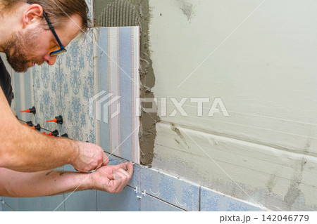 Worker Laying Ceramic Tiles on the Wall. Repairman Placing White Gray Square Tiles, Applying Adhesive. Builder Installing Tile Using Leveler, Tile Leveling Clips. Tiling. Finishing Repair Work. 4K Worker Laying Ceramic Tiles on the Wall. Repairman Placing White Gray Square Tiles, Applying Adhesive. Builder Installing Tile Using Leveler, Tile Leveling Clips. Tiling. Finishing Repair Work. 4K 142046779