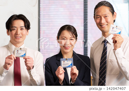 社員証を見せて笑顔で並ぶ3人のビジネスパーソン 社員証を見せて笑顔で並ぶ3人のビジネスパーソン 142047407