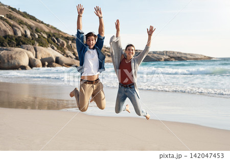 Beach, portrait and couple jump together for vacation, travel and holiday fun or quality time. Happy, man and woman by ocean with love excited for memories, relationship and bonding in California 142047453