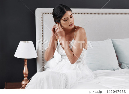 Luxury, jewellery and bride in bedroom at wedding, event or dressing in rich fashion for marriage. Bridal, style and girl in gown on bed with vintage, retro or diamond earrings in outfit at hotel 142047488