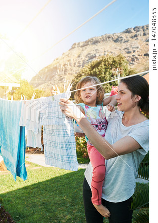 Backyard, mom and child hanging laundry together with help, teaching and learning chores. Housekeeping, mother and daughter with clean clothes on line outside to sun dry with home, care and bonding. 142048355