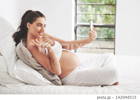 Pregnant woman, phone selfie or video call in home bedroom for communication or online consultation. Wave, mom or happy mother with mobile app for gynecology telehealth, pregnancy update or maternity Pregnant woman, phone selfie or video call in home bedroom for communication or online consultation. Wave, mom or happy mother with mobile app for gynecology telehealth, pregnancy update or maternity 142048515