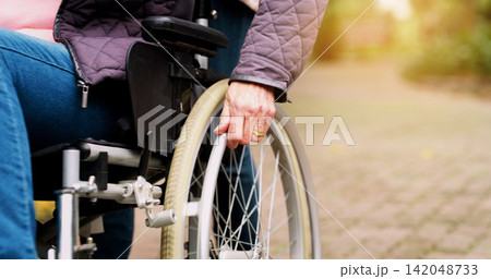 Park, wheelchair and hand of person with a disability for retirement, support and healthcare. Nature, path and elderly man with mobility aid for travel, morning adventure and assistance in garden Park, wheelchair and hand of person with a disability for retirement, support and healthcare. Nature, path and elderly man with mobility aid for travel, morning adventure and assistance in garden 142048733