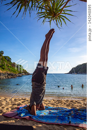 A man doing yoga in headstand pose on Yanui Beach. 142048895