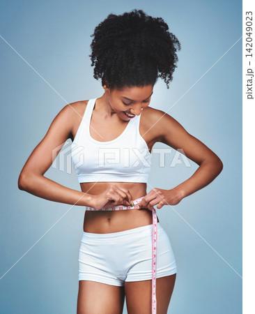 Girl, happy and tape on stomach in studio to measure weight loss, progress of diet and daily exercise. Woman, grey background and measurement for improvement of new prescription drug or tummy tuck. Girl, happy and tape on stomach in studio to measure weight loss, progress of diet and daily exercise. Woman, grey background and measurement for improvement of new prescription drug or tummy tuck. 142049023