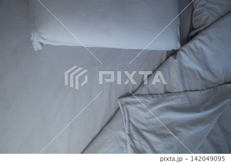 An overhead view of a bed with two pillows, covered with gray linens, lies a carelessly folded blanket, forming soft folds. The concept: an atmosphere of comfort and relaxation, going to bed. High 142049095