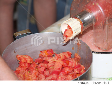 Traditional homemade tomato processing with a manual grinder, turning fresh ripe tomatoes into smooth pulp for sauce, puree, and food preservation in a home kitchen. Traditional homemade tomato processing with a manual grinder, turning fresh ripe tomatoes into smooth pulp for sauce, puree, and food preservation in a home kitchen. 142049101