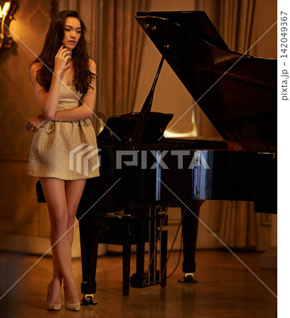 Ballroom, woman and thinking with piano, musician and mansion ready for music performance. Elegant, lounge and instrument with chandelier, pianist and luxury with sound artist and classy fashion Ballroom, woman and thinking with piano, musician and mansion ready for music performance. Elegant, lounge and instrument with chandelier, pianist and luxury with sound artist and classy fashion 142049367