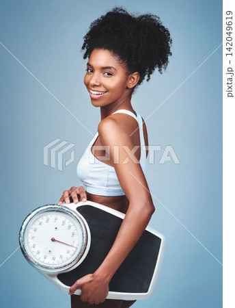 Black girl, portrait and scale in studio to weigh, confident measure and blue background. Female person, fitness and diet for balance, exercise results and proud of weight loss success and health Black girl, portrait and scale in studio to weigh, confident measure and blue background. Female person, fitness and diet for balance, exercise results and proud of weight loss success and health 142049619
