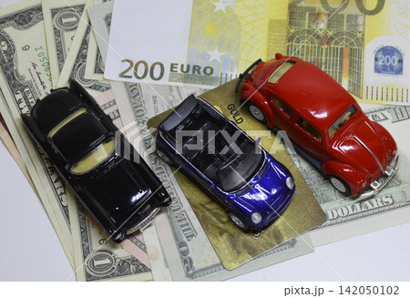 Three toy cars placed on top of US dollar and euro banknotes. 142050102