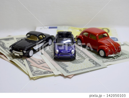 Three toy cars placed on top of US dollar and euro banknotes. 142050103