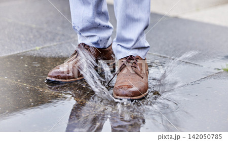 Person, puddle and shoe stepping in water on ground for commute to work, job or business. Splash, street and wet footwear with employee in city for travel, progress or weather resistant attitude 142050785
