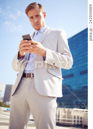 Portrait, phone and serious businessman in city for travel, commute and typing outdoor in low angle. Mobile, professional and consultant in street for social media, network and scroll online in USA Portrait, phone and serious businessman in city for travel, commute and typing outdoor in low angle. Mobile, professional and consultant in street for social media, network and scroll online in USA 142050869