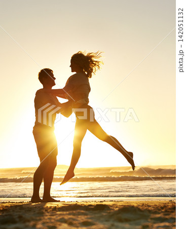 Lifting, sunset and couple with love at beach, ocean or sea for affection, bonding or for fun with soulmate. People, sunrise and romance for care together on vacation, holiday and travel in Australia 142051132