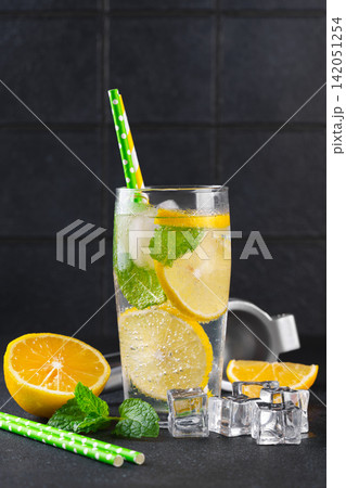 Fresh homemade lemonade with lemon slices, mint and ice in glasses on black kitchen tile background Fresh homemade lemonade with lemon slices, mint and ice in glasses on black kitchen tile background 142051254