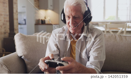 Headphones, senior man and joystick for video game, online streaming and relax for retirement at home. Technology, elderly person and happiness with smile from esports, gaming and challenge on sofa 142051359