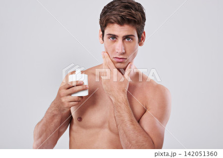 Handsome man, portrait and grooming with aftershave, skincare cosmetics or lotion on a gray studio background. Young male person or model with beauty cream or container for hygiene on mockup space Handsome man, portrait and grooming with aftershave, skincare cosmetics or lotion on a gray studio background. Young male person or model with beauty cream or container for hygiene on mockup space 142051360