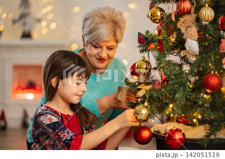 Grandmother and granddaughter decorating Christmas tree for holidays 142051519