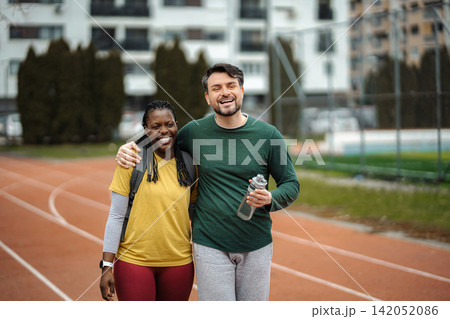Diverse couple smiling after working out on running track Diverse couple smiling after working out on running track 142052086
