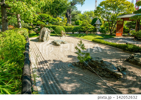Princess Grace Japanese Garden  in Monaco in summer and pond  and pavilion, carps KOI and stone lantern in water . Red flowers of lantana  (from America continent) 142052632