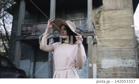 Young woman adjusting a wide-brim hat beside an old city facade Young woman adjusting a wide-brim hat beside an old city facade 142053357