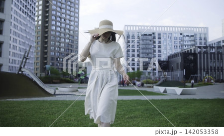 Woman walking across a city park in a light summer dress Woman walking across a city park in a light summer dress 142053358