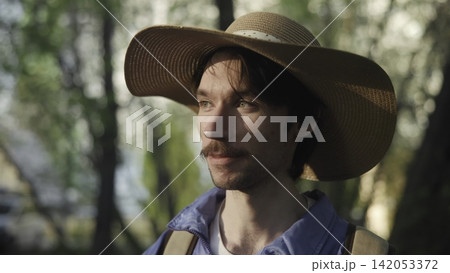Young man in a straw hat standing outdoors in warm sunlight with forest background Young man in a straw hat standing outdoors in warm sunlight with forest background 142053372