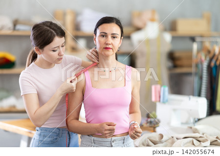 Female tailor measures a girl size with tape to create new dress Female tailor measures a girl size with tape to create new dress 142055674