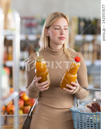 Girl buyer examine goods, choose peach juice in store Girl buyer examine goods, choose peach juice in store 142055677