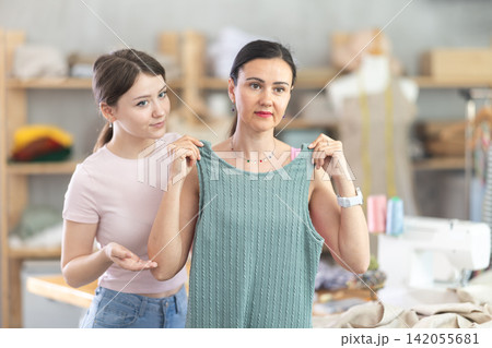 Female tailor helps client try on summer dress in sewing workshop Female tailor helps client try on summer dress in sewing workshop 142055681