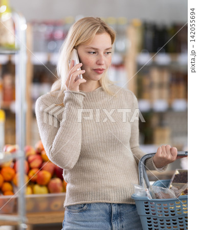 Female shopper talking on mobile phone while shopping in supermarket Female shopper talking on mobile phone while shopping in supermarket 142055694