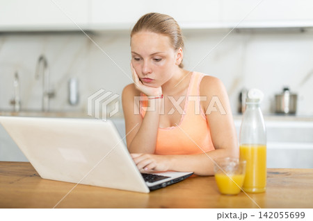 Teenage girl working on laptop while sitting at table in kitchen Teenage girl working on laptop while sitting at table in kitchen 142055699