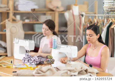 Two seamstresses working on sewing machines in sewing workshop Two seamstresses working on sewing machines in sewing workshop 142055724