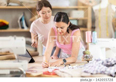 Using ruler and chalk, women tailor draws dress diagram scheme on paper Using ruler and chalk, women tailor draws dress diagram scheme on paper 142055728