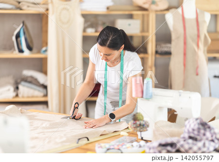 Woman seamstress cutting fabric in sewing workshop Woman seamstress cutting fabric in sewing workshop 142055797