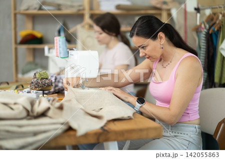 Sewing workshop work - female tailors sewing dresses on sewing machines Sewing workshop work - female tailors sewing dresses on sewing machines 142055863
