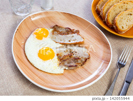 Appetizing breakfast with scrambled eggs and juicy bacon closeup Appetizing breakfast with scrambled eggs and juicy bacon closeup 142055944