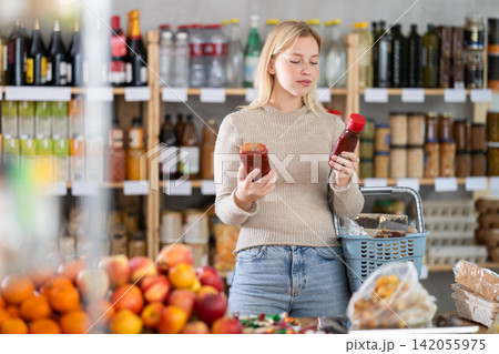 Girl shopping at supermarket - choosing ketchup in grocery supermarket Girl shopping at supermarket - choosing ketchup in grocery supermarket 142055975