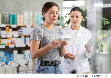 Young woman choosing ointment while pharmacist offering in drugstore Young woman choosing ointment while pharmacist offering in drugstore 142055978