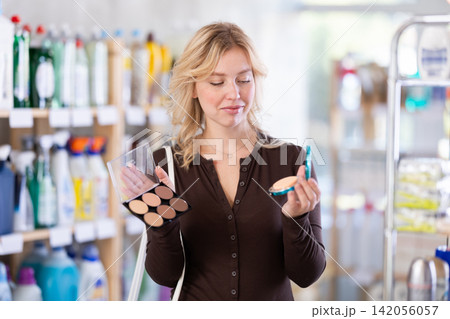 Girl housewife in cosmetic store examines goods, chooses eye shadow Girl housewife in cosmetic store examines goods, chooses eye shadow 142056057