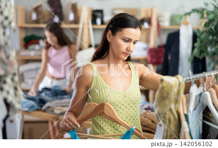 Near rack, woman buys something summer cloth, chooses items. Near rack, woman buys something summer cloth, chooses items. 142056102