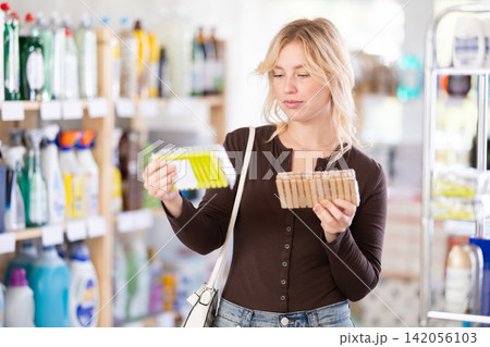 Attentive young girl choosing clothespins for home in household goods department in hypermarket 142056103