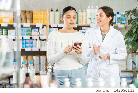 Woman showing prescription on phone to pharmacist at pharmacy Woman showing prescription on phone to pharmacist at pharmacy 142056113