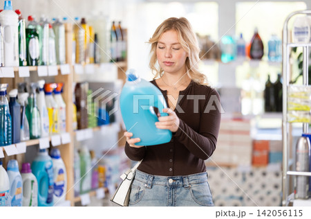 Girl housewife in household store examines goods, chooses liquid detergent 142056115