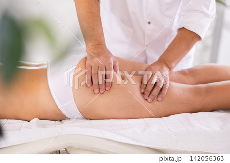 Hands of old masseur conducting hip massage for woman client 142056363