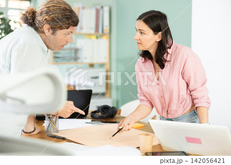 Two architects discuss a building plan in company office Two architects discuss a building plan in company office 142056421